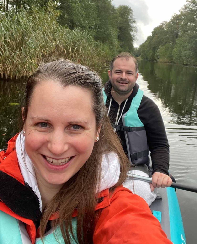 Portrait von Hanno und Kristina beim Paddeln auf der Spree mit Bäumen und Schilf im Hintergrund