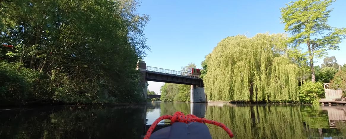 Bahnbrücke über Alsterkanal bei Kanutour in Hamburg-Winterhude und grüne Bäume am Kanalufer