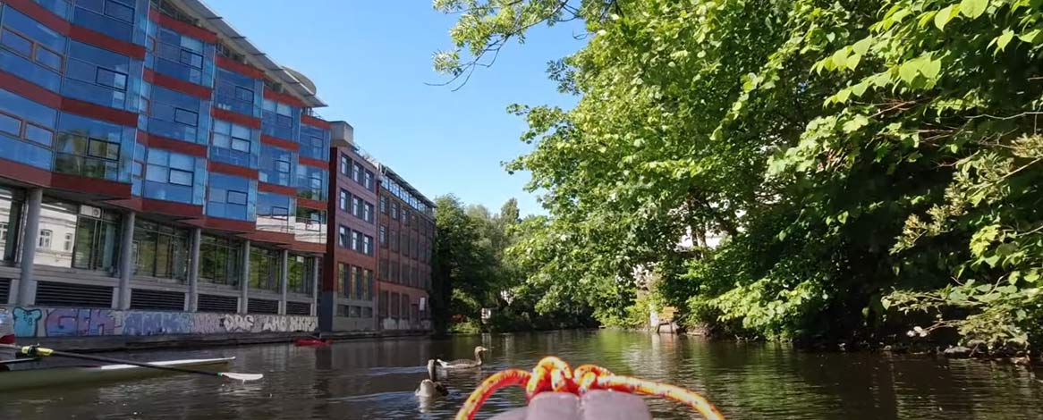 Blick auf Goldbekkanal von Kanu aus mit zwei vorm Boot schwimmenden Enten und linksseitig ein Ruderer