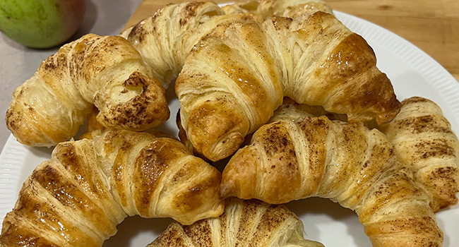 Nahaufnahme von Apfelhörnchen mit Zimt auf einem weißen Teller liegend als Teaserbild für To-Go-Rezept