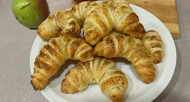 Apfelhörnchen aus Blätterteig und mit Zimt bestäubt auf einem weißen Teller liegend