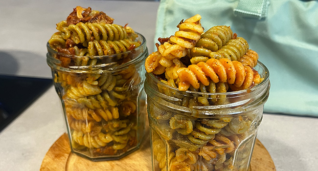 Zwei Glasbehältnisse mit Nudelsalat bestehend aus bunten Fusilli und rotem Pesto